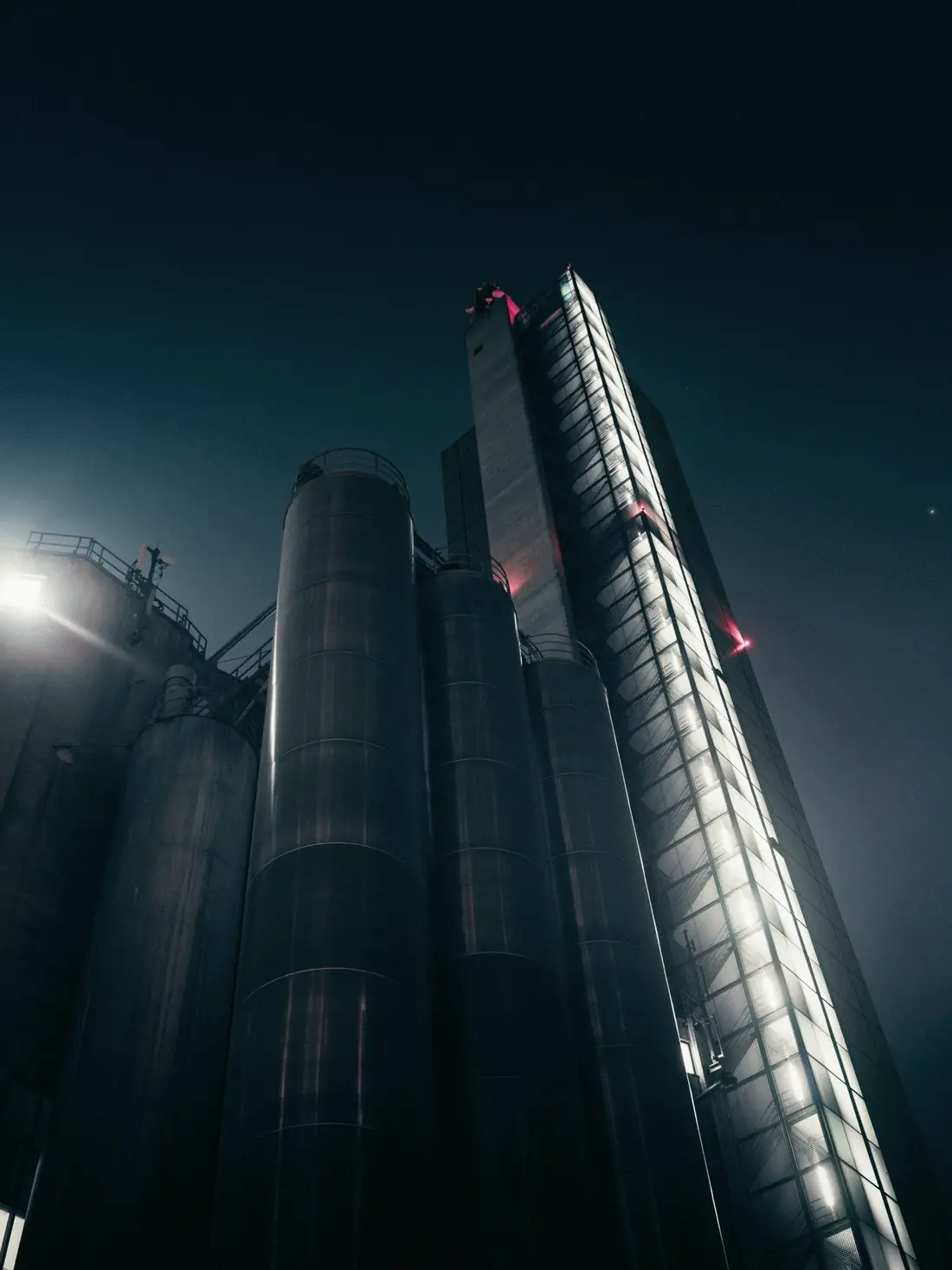 Industrial silos and a lit tower at night